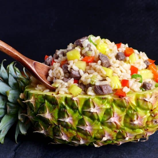 A halved and hollowed pineapple with fried rice inside