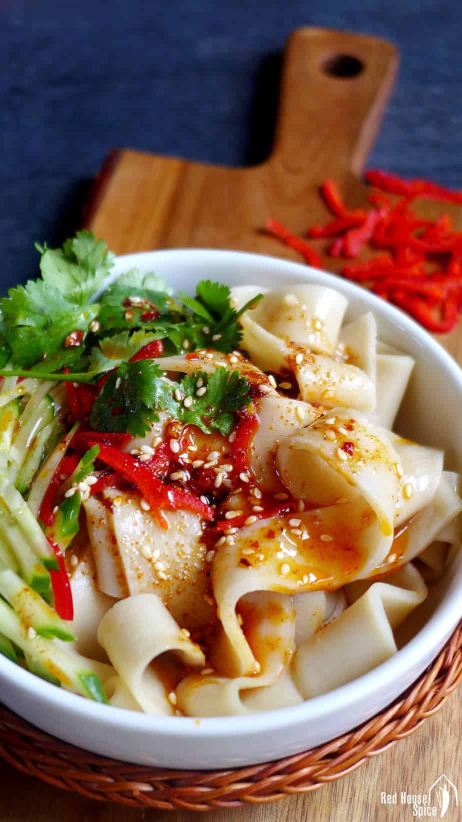 A bowl of Liang Pi (cold skin noodles) seasoned with chilli oil and sesame seeds.