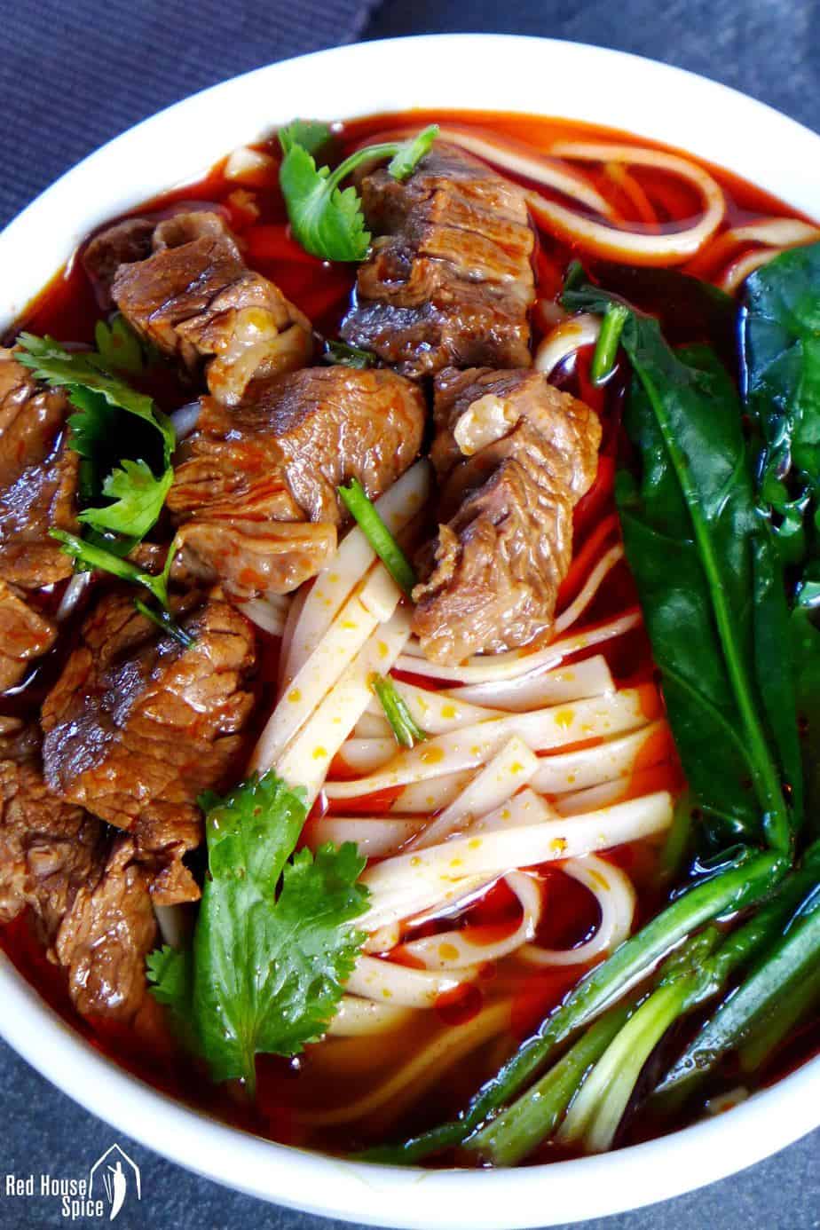 Spicy beef noodle soup: freshly cooked noodles in a spicy broth, topped with beef cubes, garnished with spinach and coriander.
