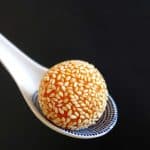A golden oranger colours sesame ball held by a ceramic spoon.