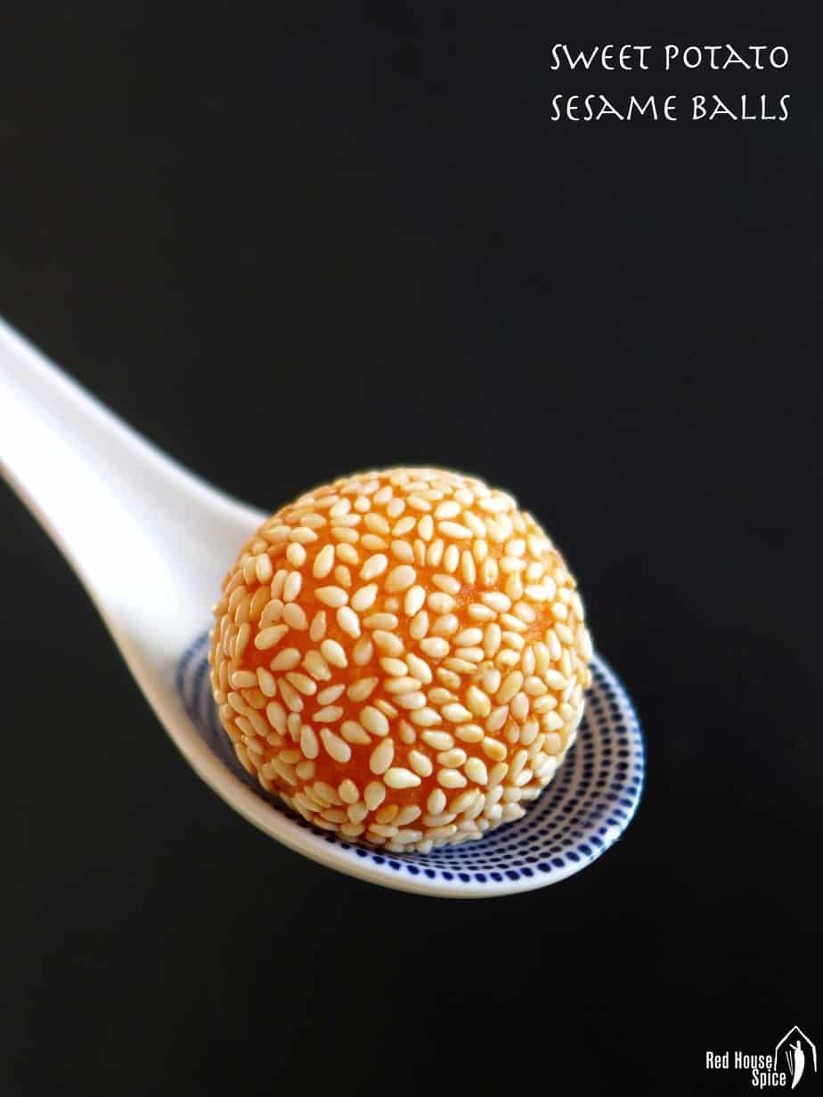 A golden oranger colours sesame ball held by a ceramic spoon.