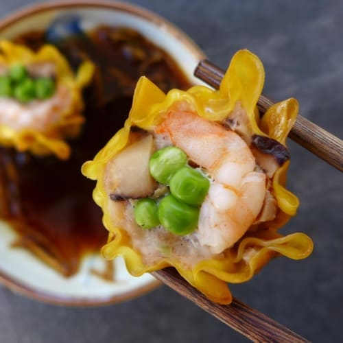 A shrimp & pork shumai held by a pair of chopsticks.