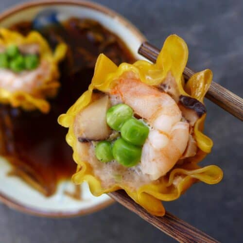 A shrimp & pork shumai held by a pair of chopsticks
