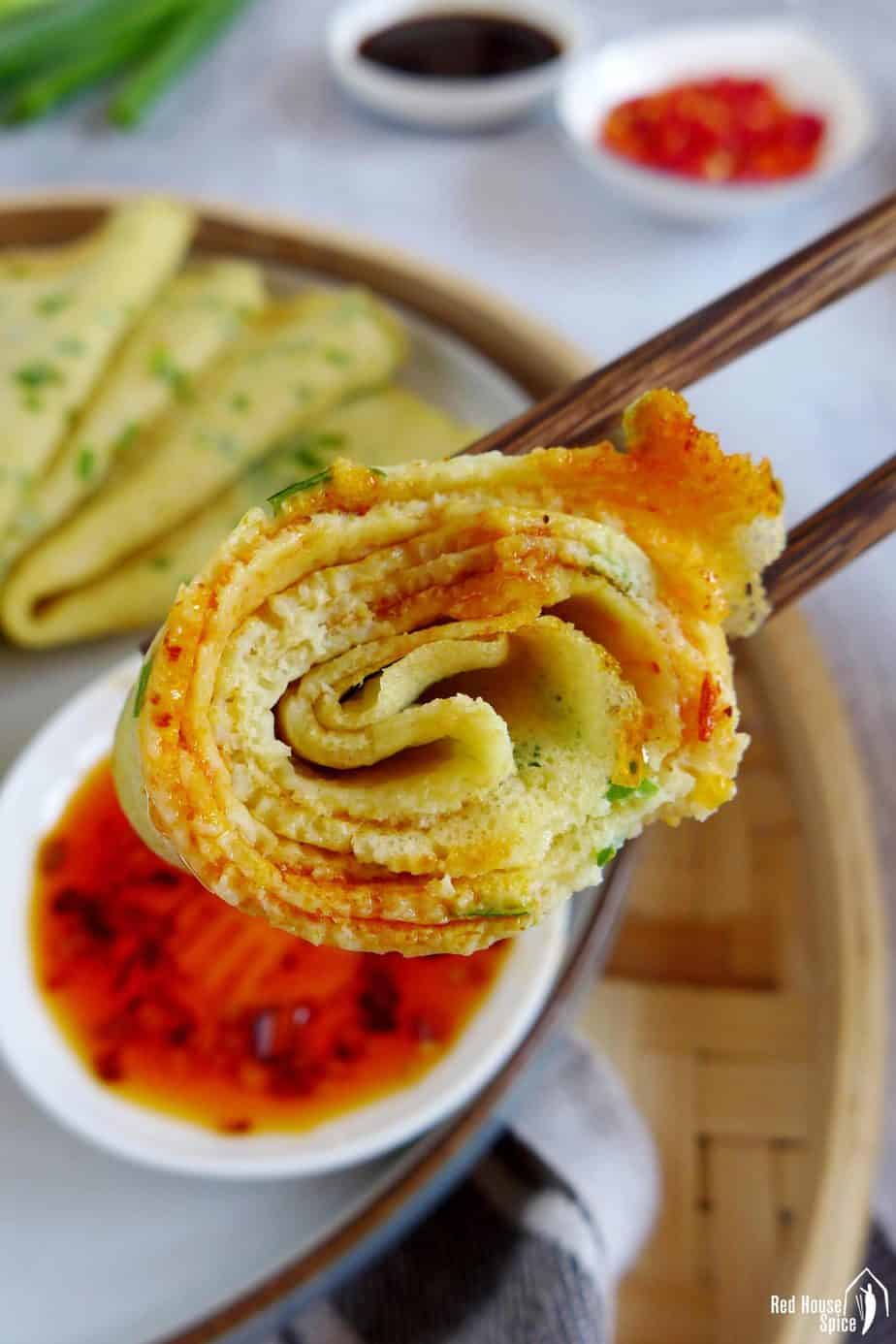 A rolled up egg & scallion crepe dipped into chili sauce