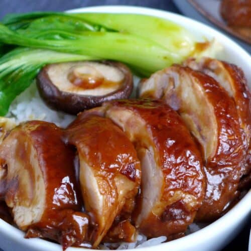 Soy sauce chicken over a bowl of rice with some vegetables