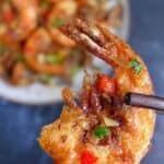 A piece of salt and pepper shrimp held by chopsticks