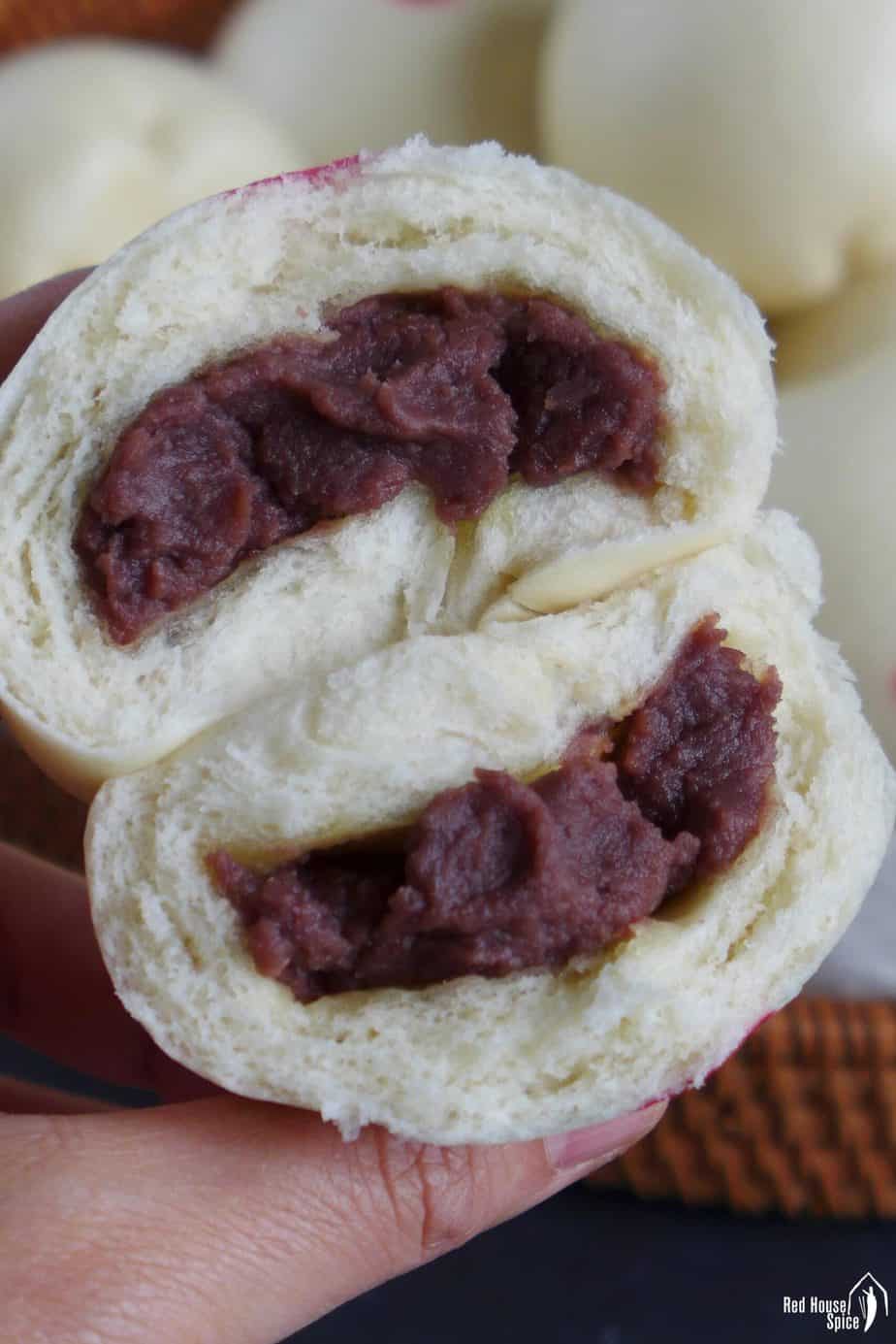 A steamed bun halved showing the red bean paste filling