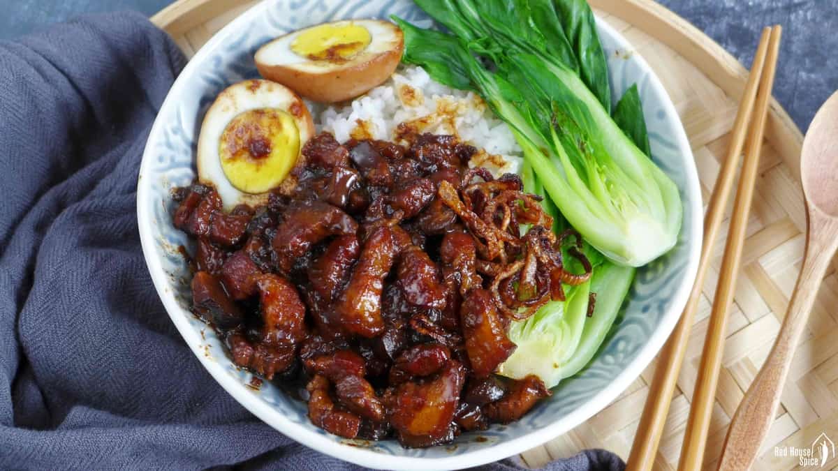 A bowl of rice with braised pork, hard boiled eggs and bok choy on top