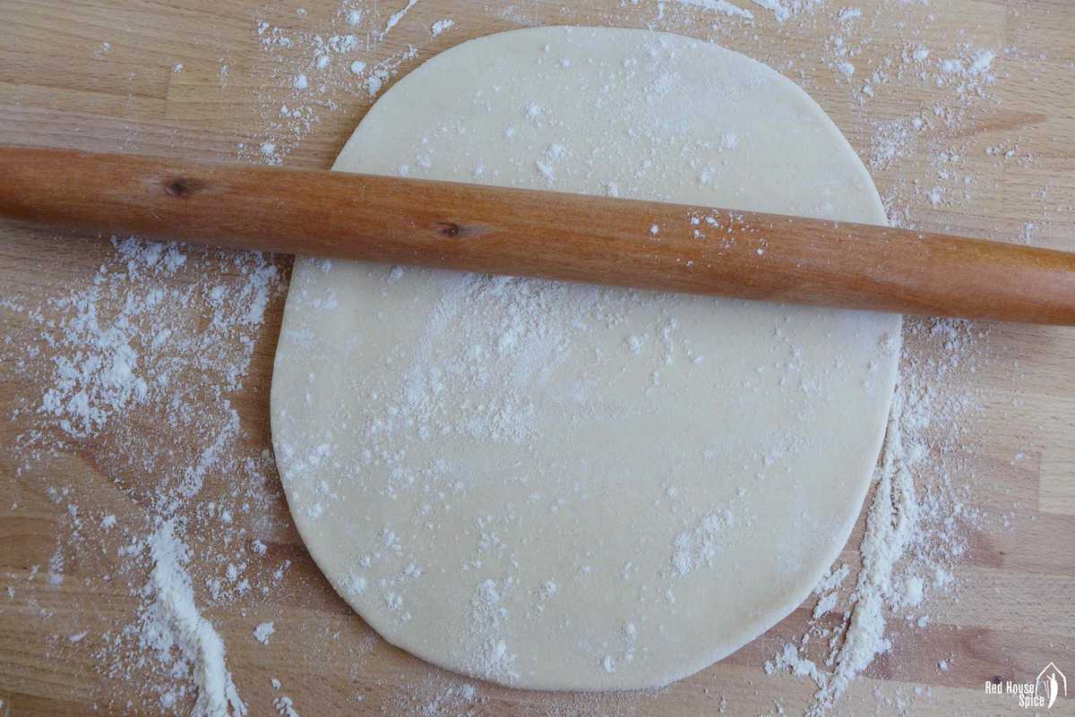 A rolling pin over a piece of flattened dough