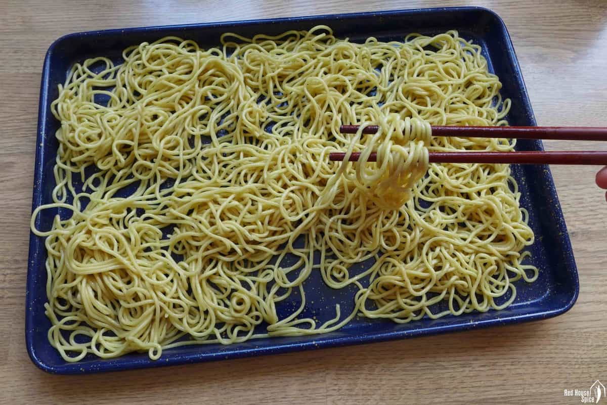 cooked noodles on a tray lifted by chopsticks