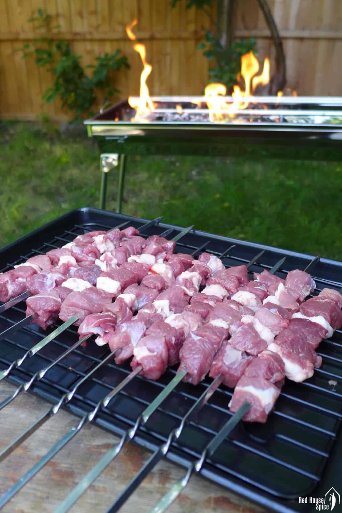 Raw lamb on skewers with a rectangle grill in the background