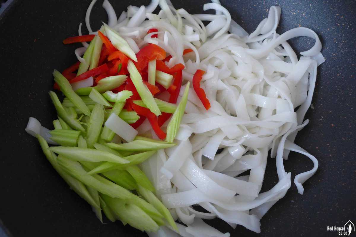 wide rice noodles, onion, celery and bell pepper in a wok