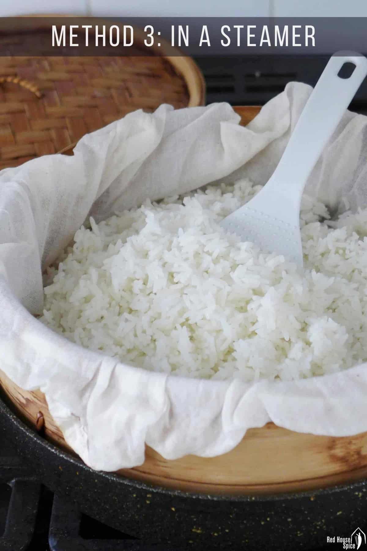 Cooked jasmine rice in a bamboo steamer over a piece of muslin cloth.