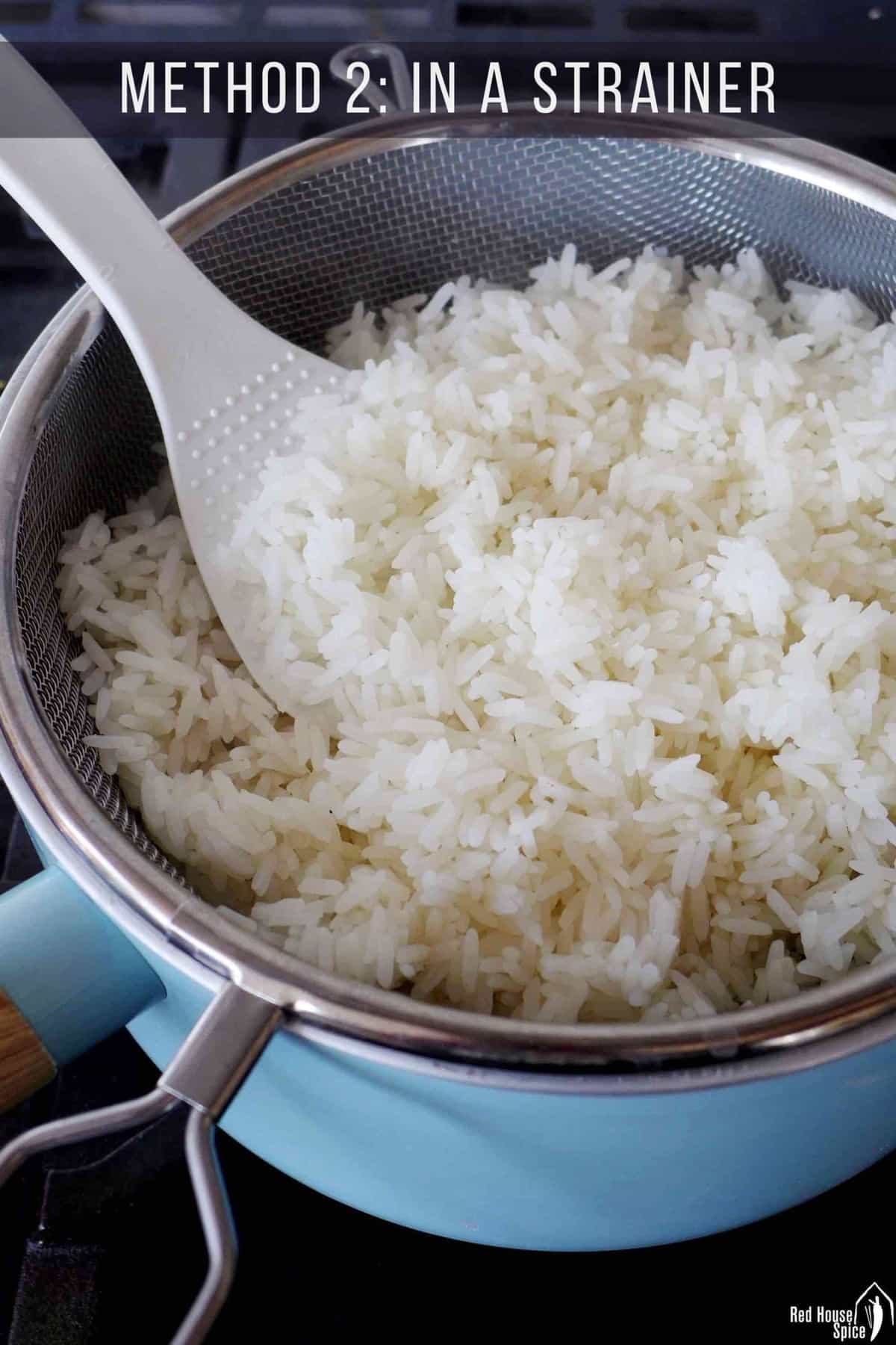 Cooked jasmine rice in a strainer over a saucepan.