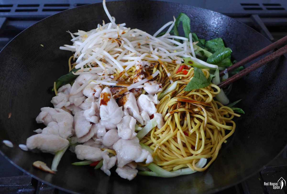 chicken, veggies, noodles and sauce in a wok.