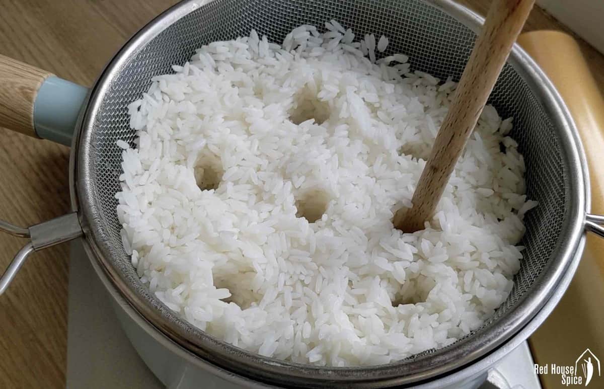 Poking holes in rice inside a strainer.