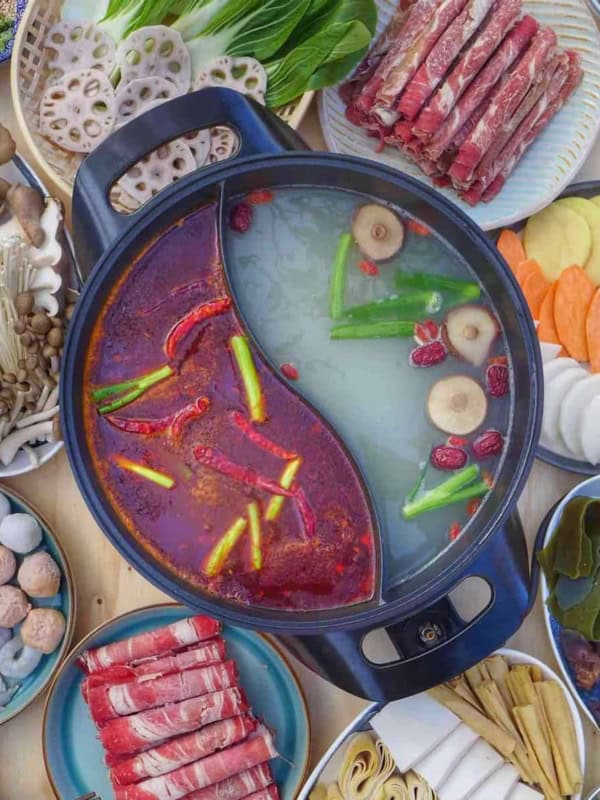 A divided hot pot surrounded with various raw ingredients