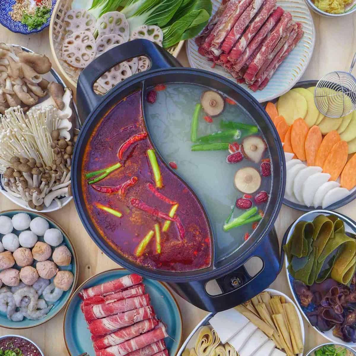 A divided hot pot surrounded with various raw ingredients
