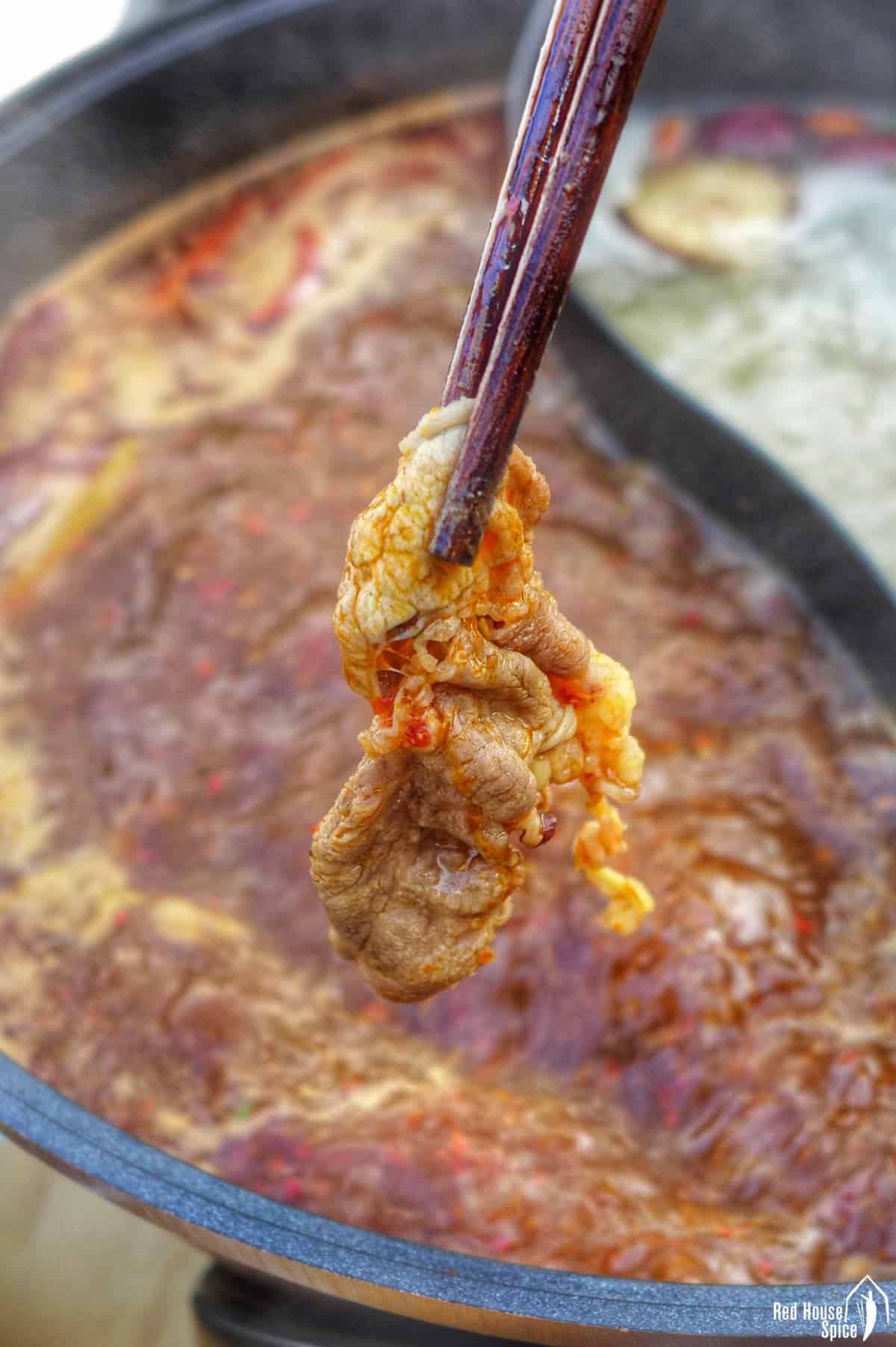 chopsticks holding a piece of meat over a hot pot