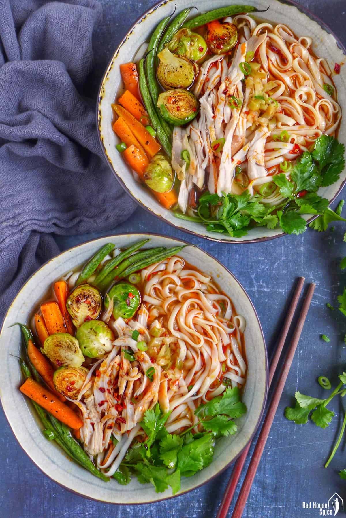 Two bowls of noodle soup made with Christmas leftovers, such as shredded turkey, Brussels sprouts, carrots and green beans.