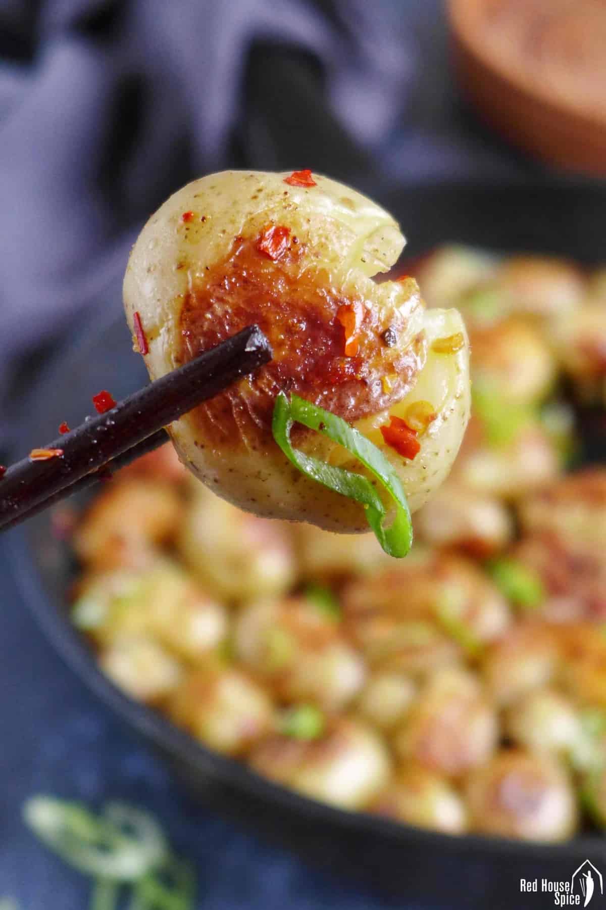 A pan-fried baby potatoes held by chopsticks