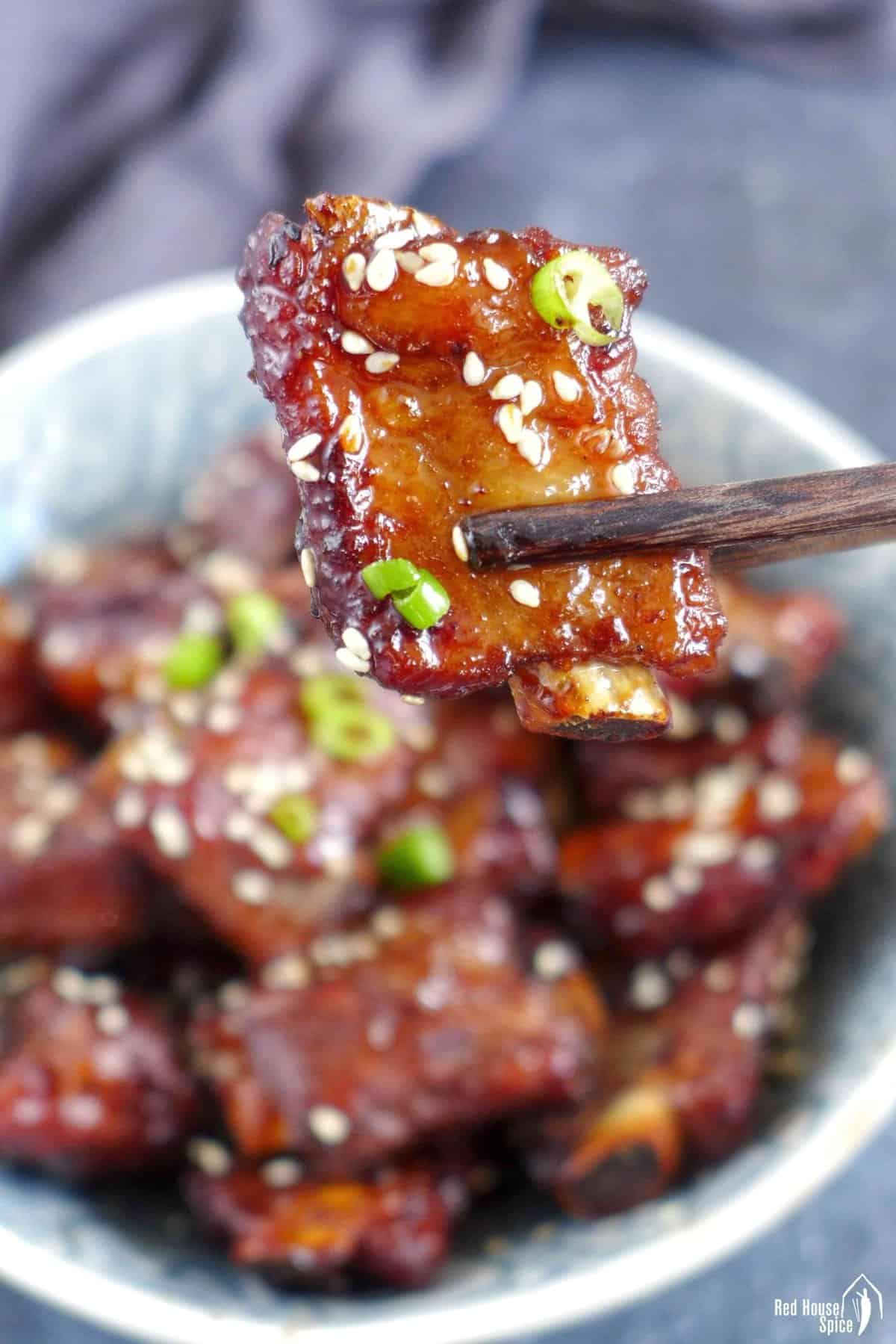 A piece of sweet and sour rib held by chopsticks