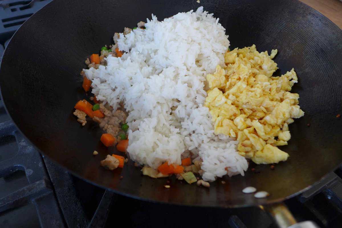 adding cooked rice and eggs to a wok