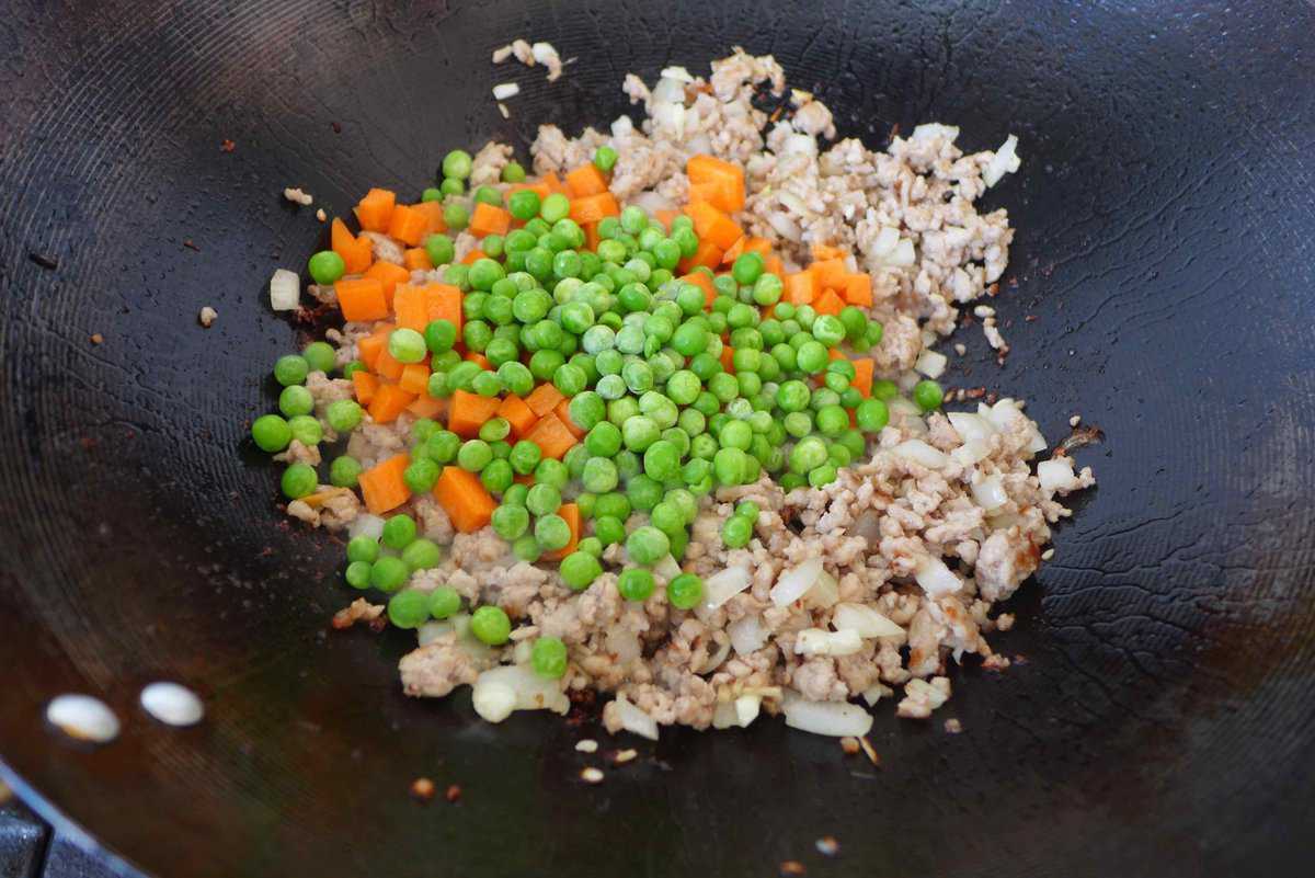 adding peas and carrots to pork