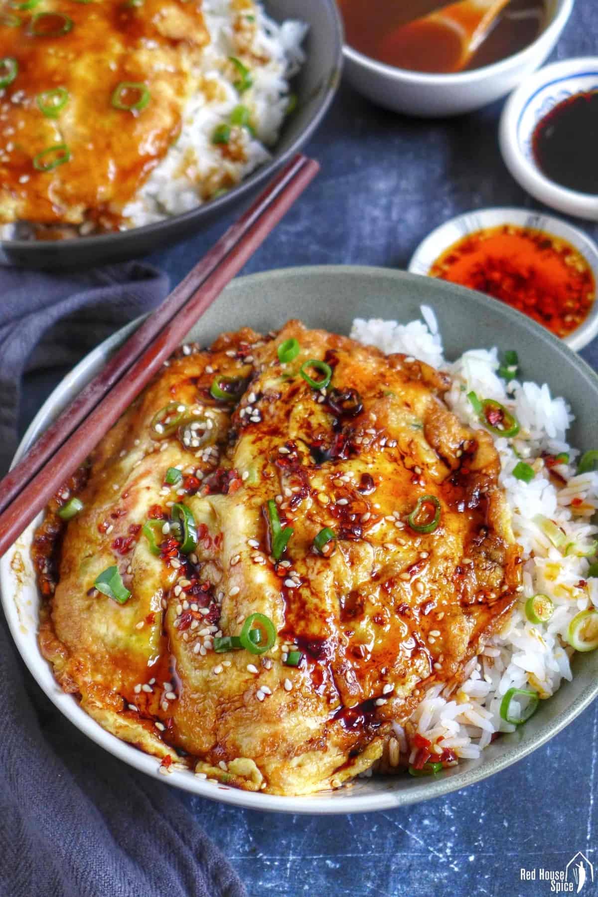 Chinese egg foo young over rice with chilli oil and soy sauce on top.