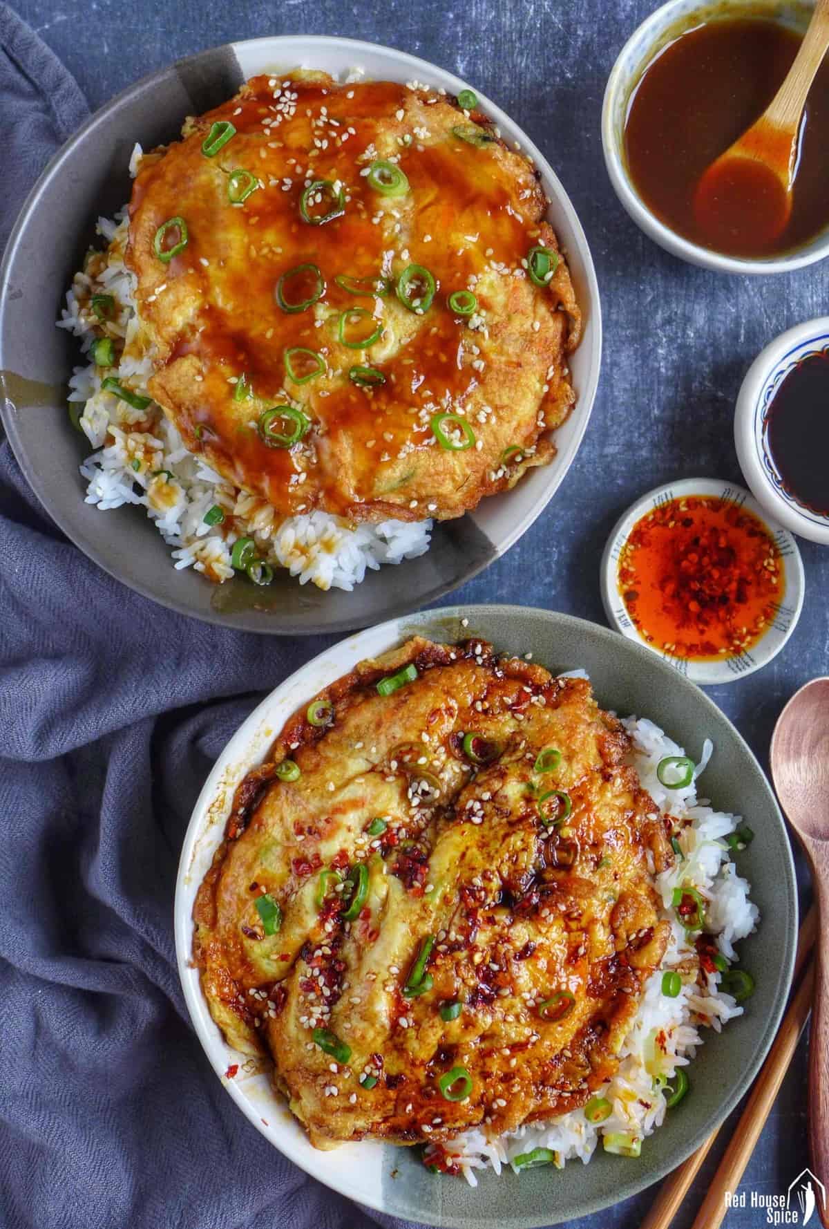 two pieces of egg foo young over rice. One with gravy, the other with chilli oil and soy sauce.