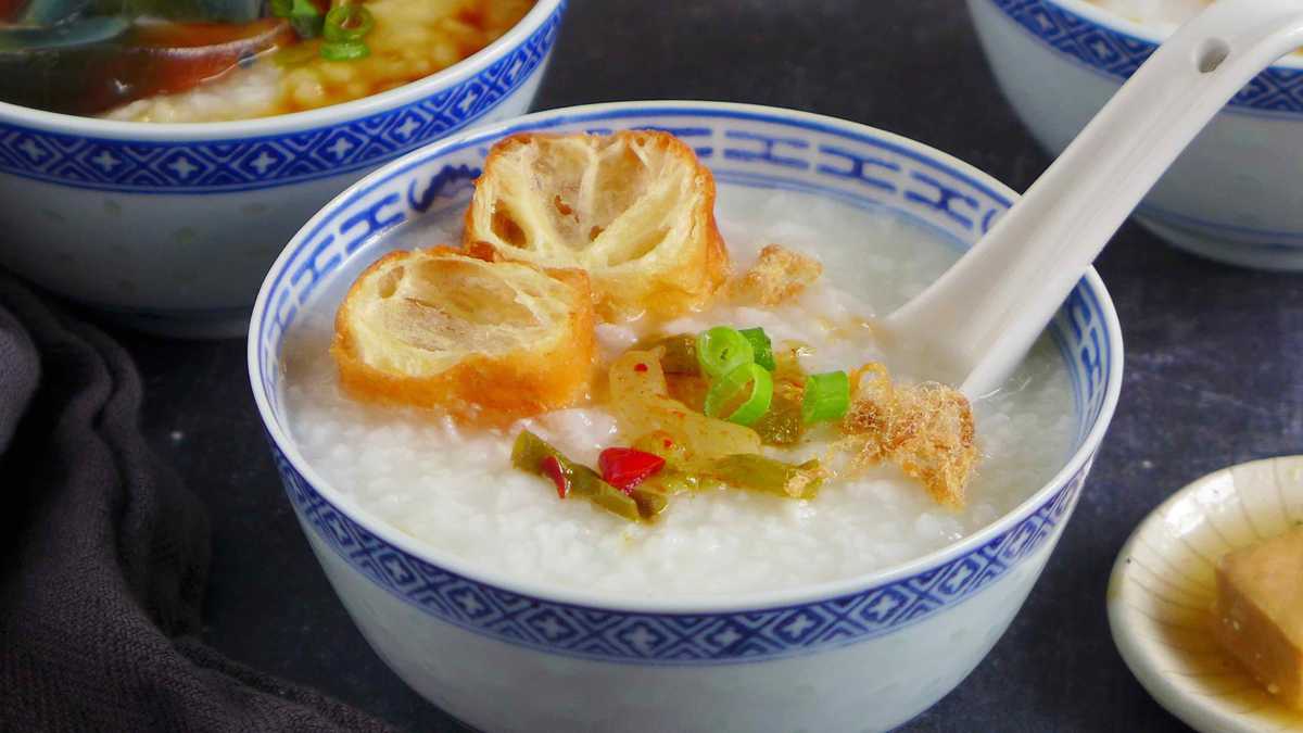 a bowl of plain congee with toppings like fried dough, preserved mustard stem and pork floss
