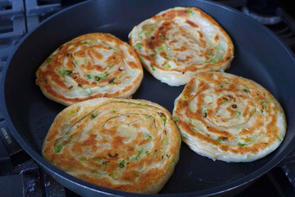 four cooked pancakes in a frying pan