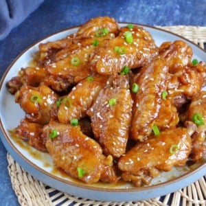 a plate of chicken wings garnished with scallions and sesame seeds