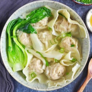 A bowl of wonton soup garnished with Bok Choy and scallions.