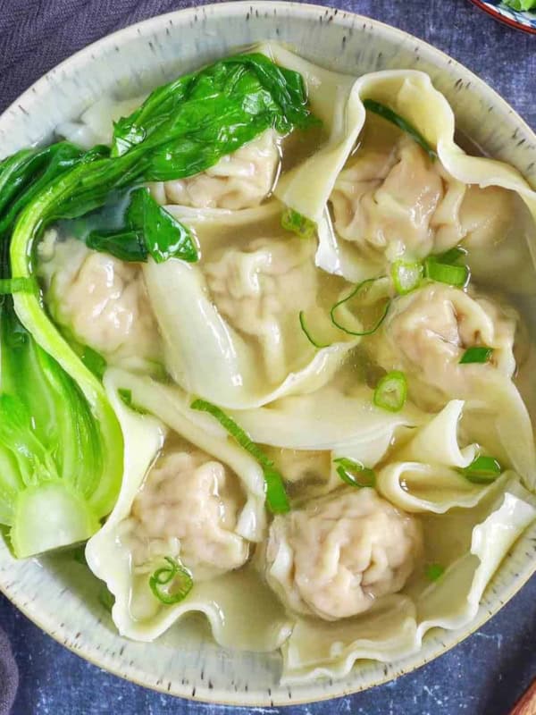 A bowl of wonton soup garnished with Bok Choy and scallions.