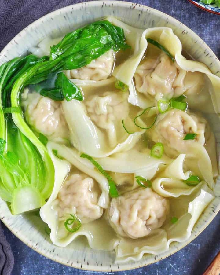 A bowl of wonton soup garnished with Bok Choy and scallions.