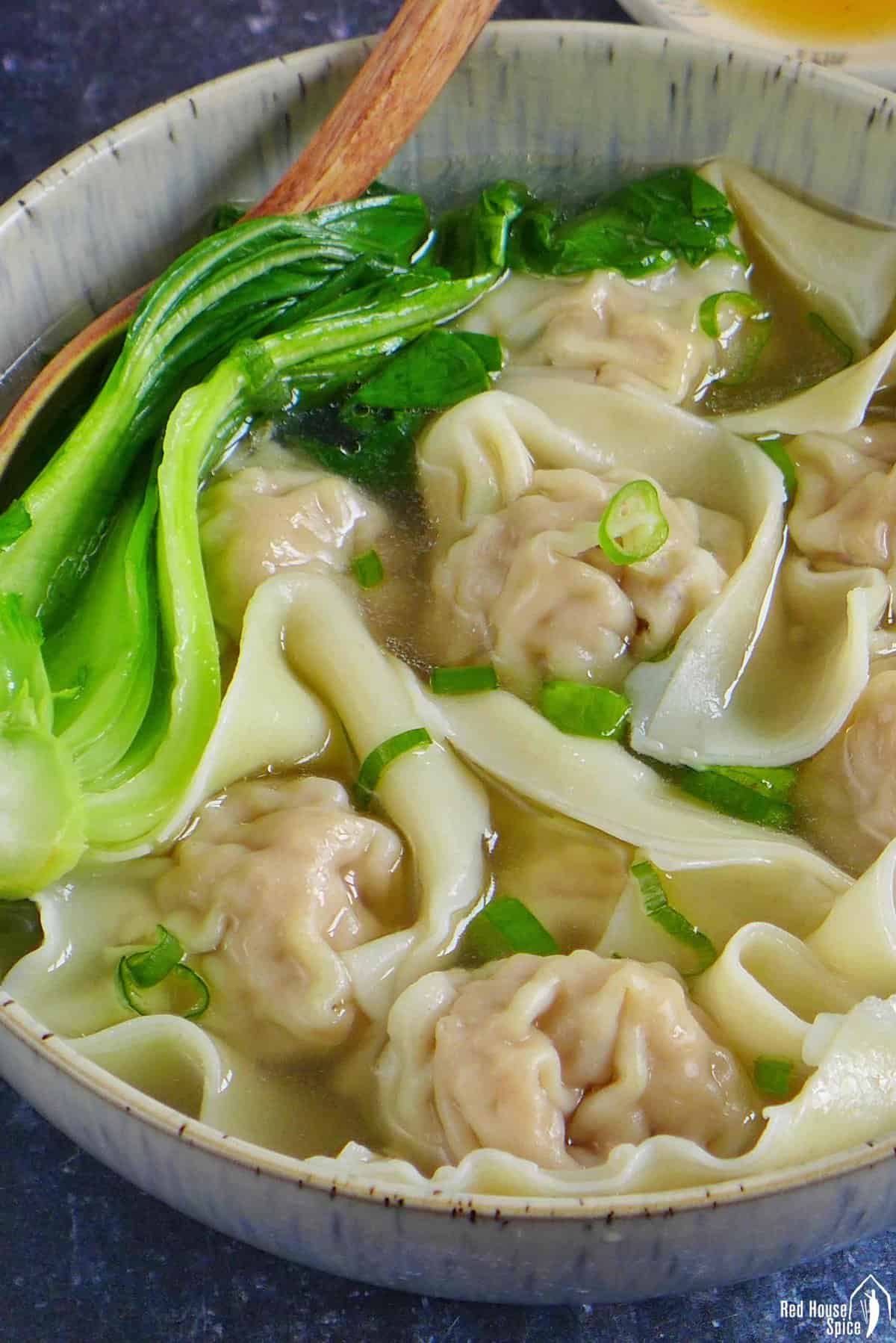 A bowl of wonton soup with Bok Choy and scallions.