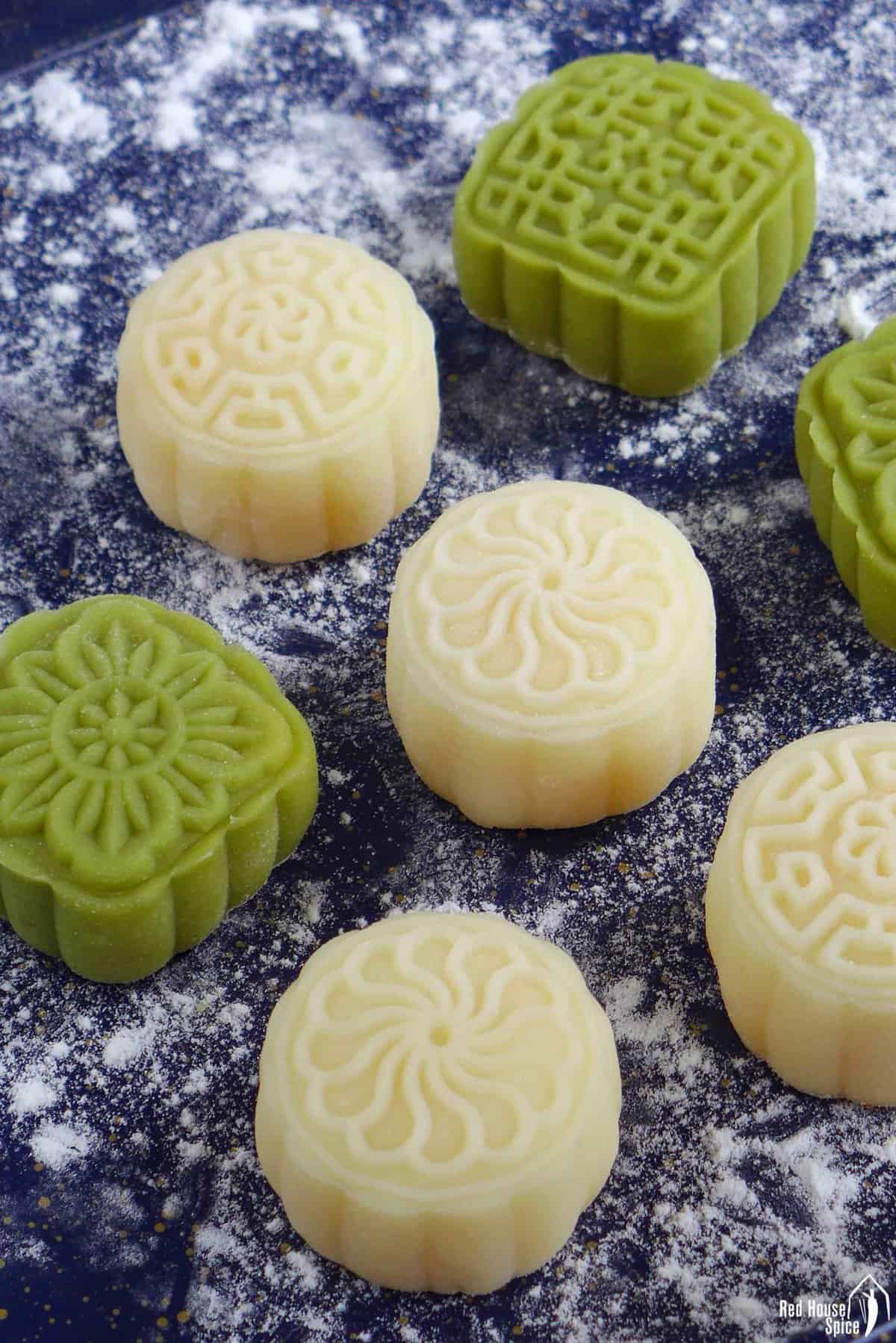 white and green Snow Skin Mooncakes on a dusted surface.