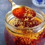 Chili oil in a spoon over a jar.