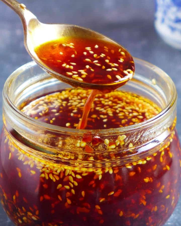 Chili oil in a spoon over a jar.