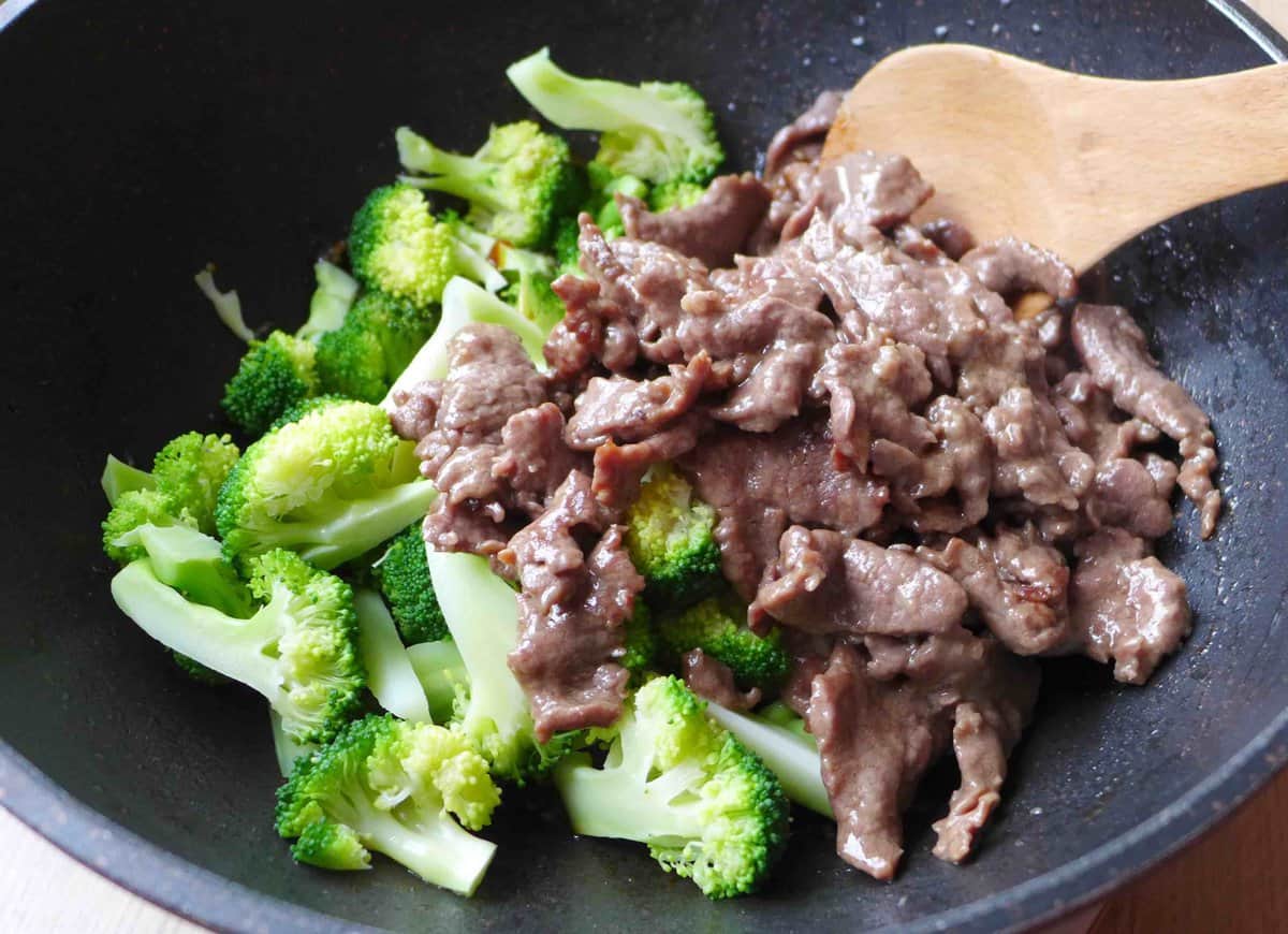 blanched broccoli and seared beef in a wok.