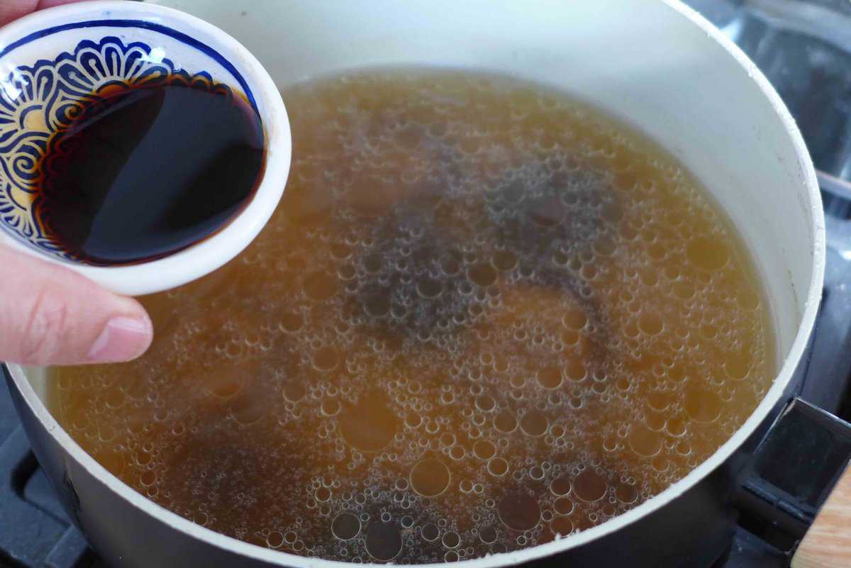 Adding soy sauce to chicken broth.