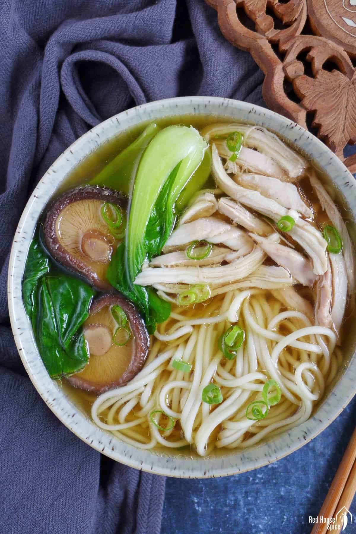 a bowl of chicken noodle soup with shiitake mushrooms and bok choy.
