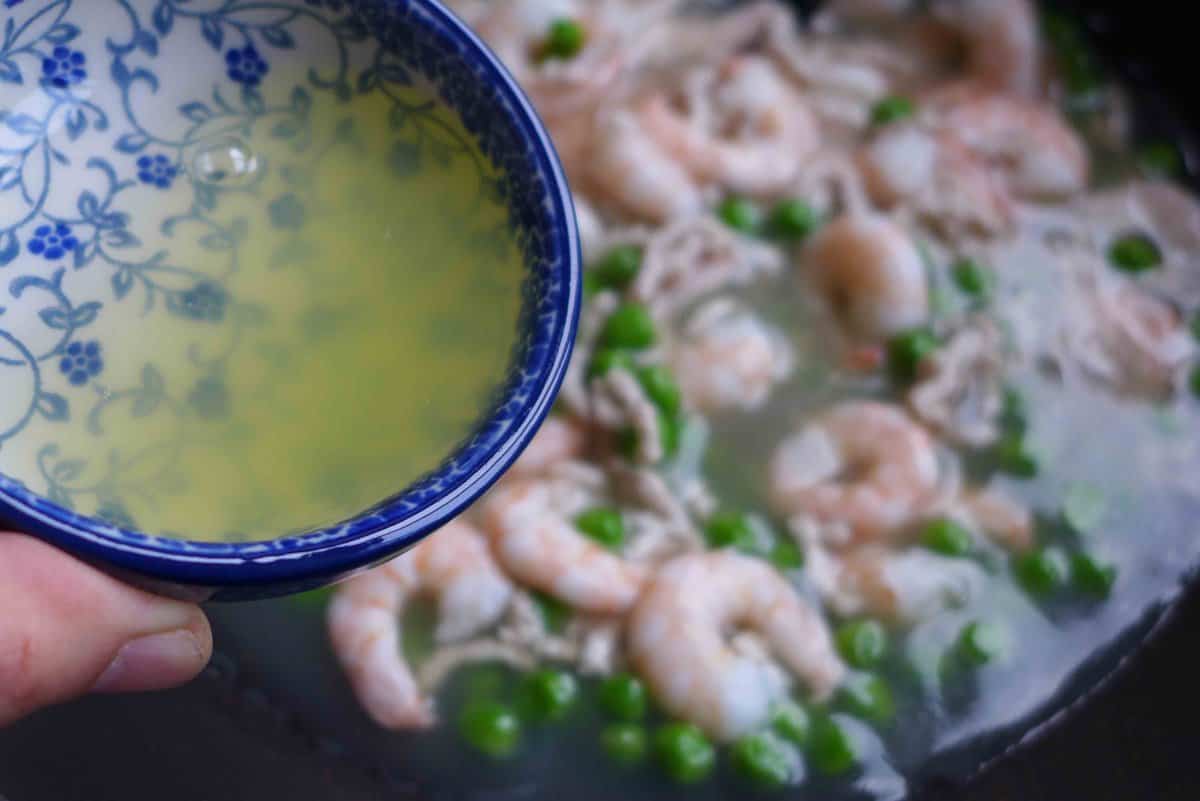 pouring egg white to shrimp and peas.