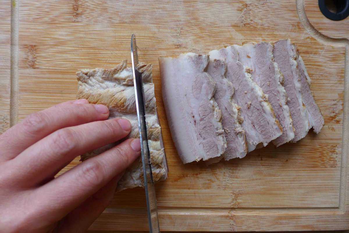 cutting a block of cooked pork belly into slices.