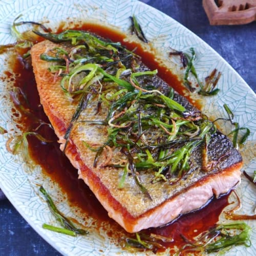 Cooked salmon filet over a dark sauce and topped with fried scallions and ginger.
