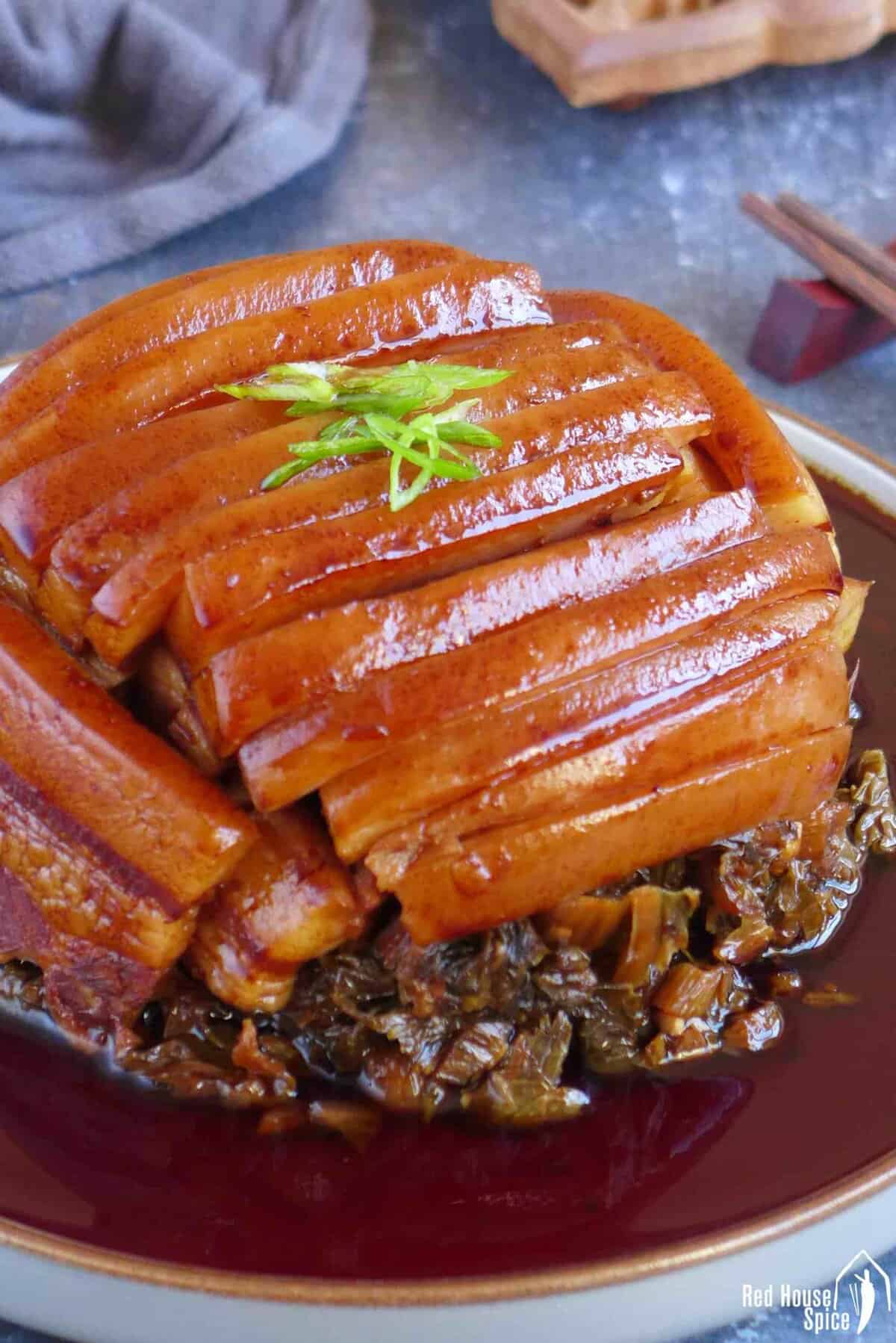 pork belly sliced over a bed of preserved mustard with sauce around.