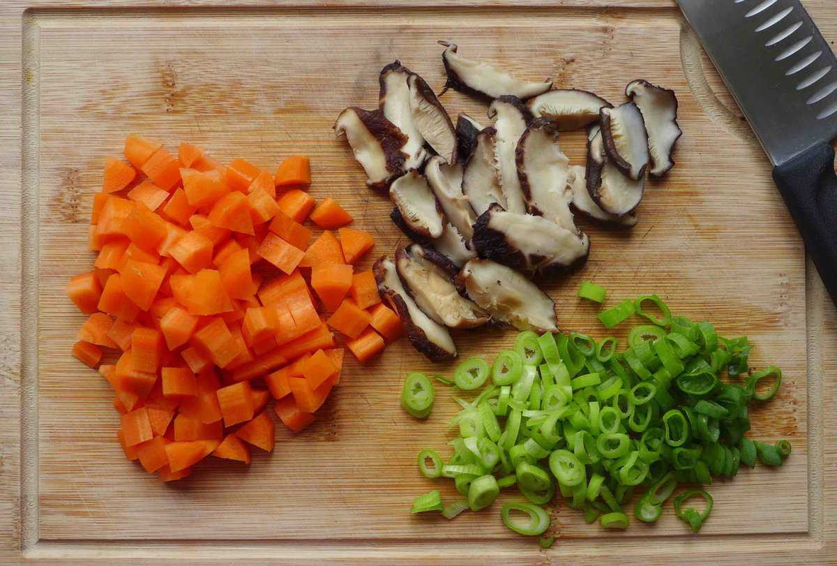 carrots, mushroom and scallions on a chopping board.