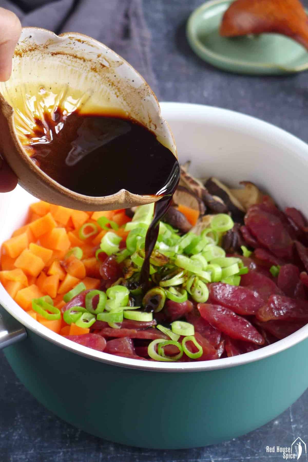 Pouring sauce over steamed Chinese sausage and vegetables.