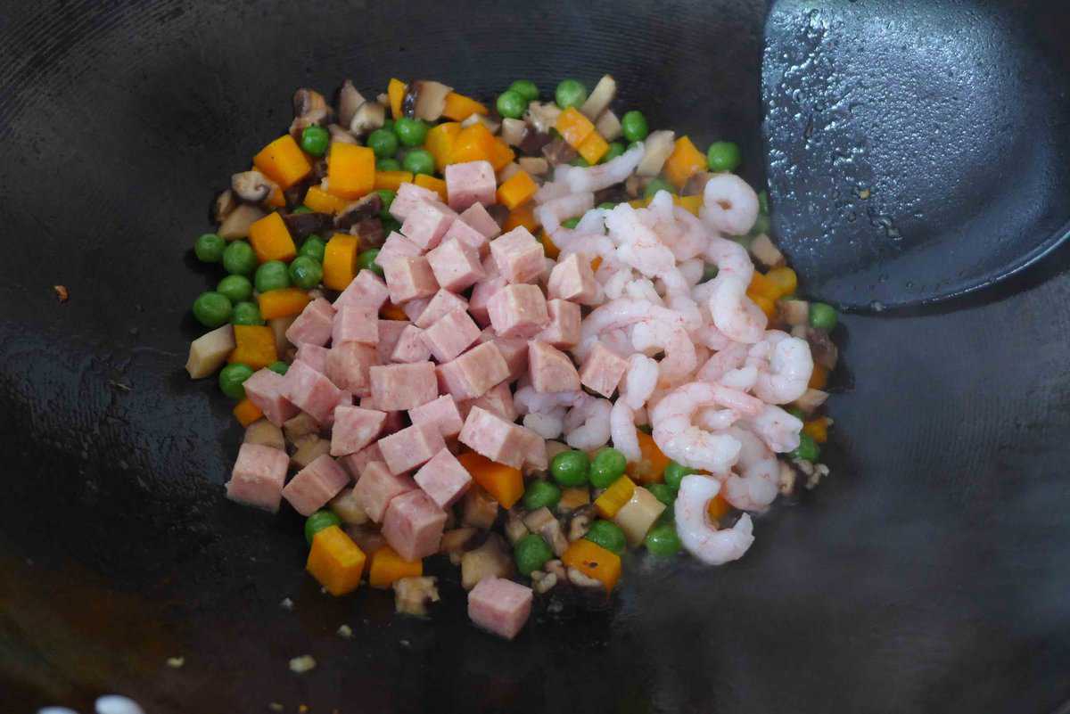 adding spam and shrimp to vegetables in a wok.